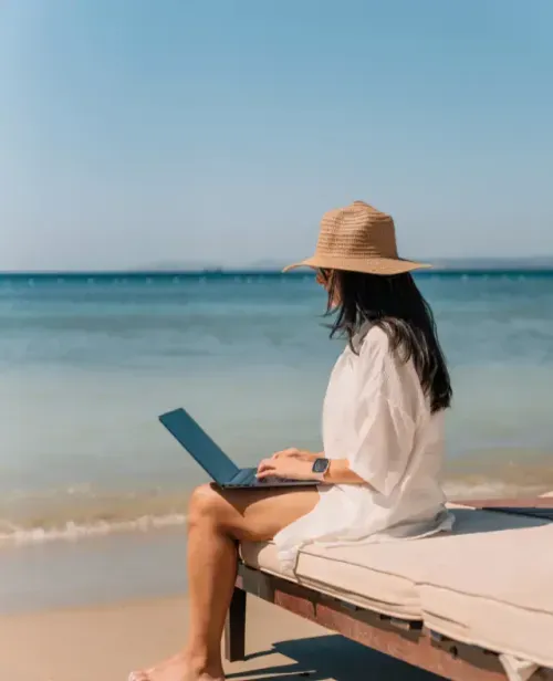 Vrouw met laptop op een ligbed aan zee